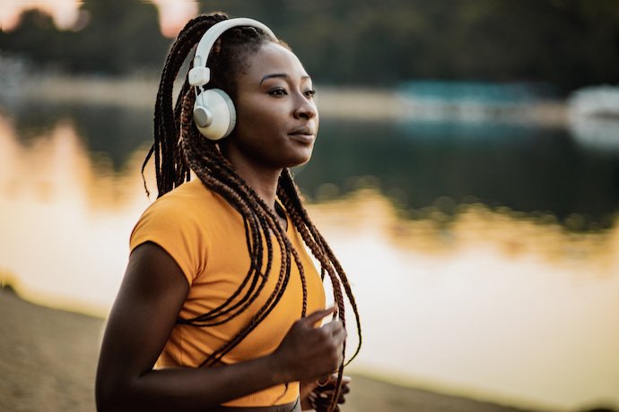 Mulher de headphones correndo na beira de um lago.