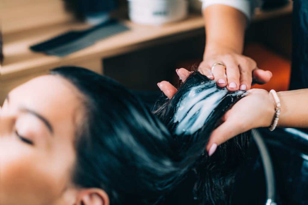 Cabeleireira passando condicionador em uma mecha de cabelo.