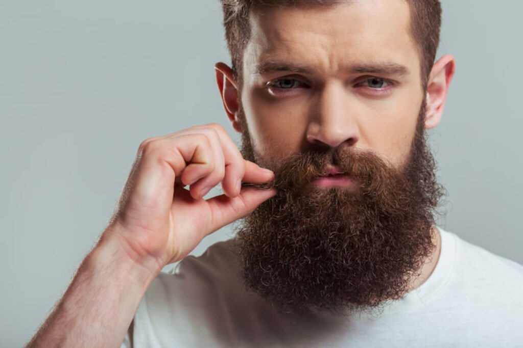Homem barbudo segurando parte do bigode.