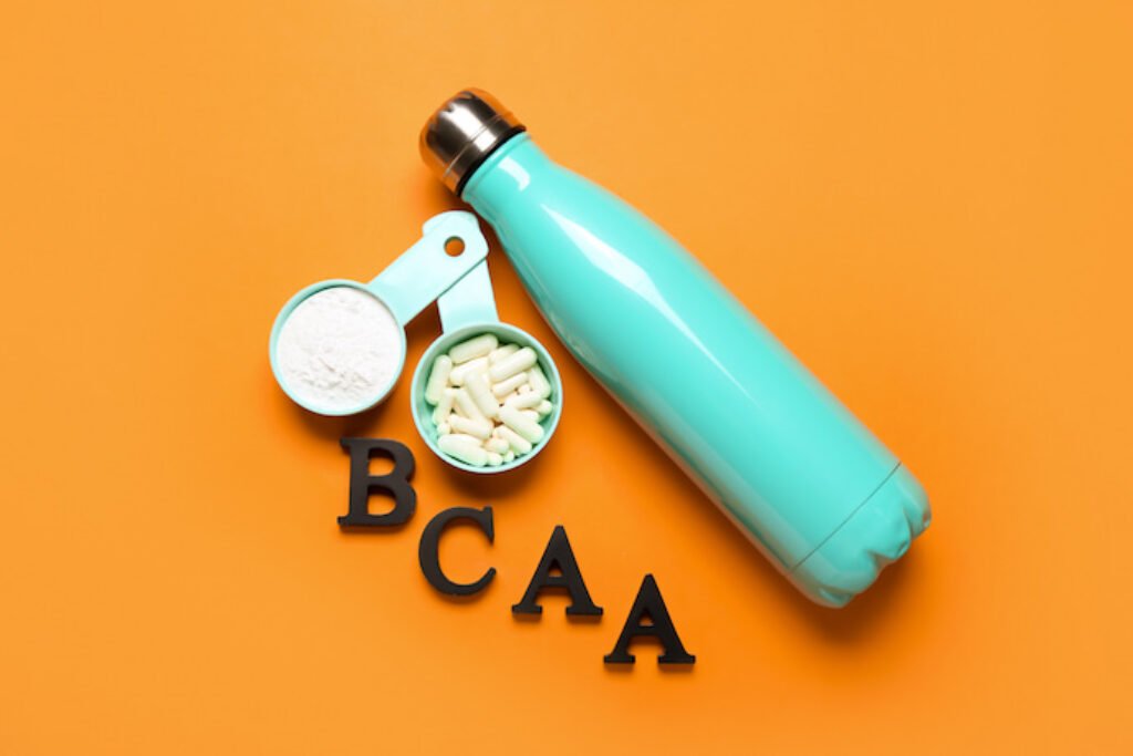 Scoops de BCAA em pó e em comprimido, uma garrafa e "BCAA" escrito em um fundo laranja.