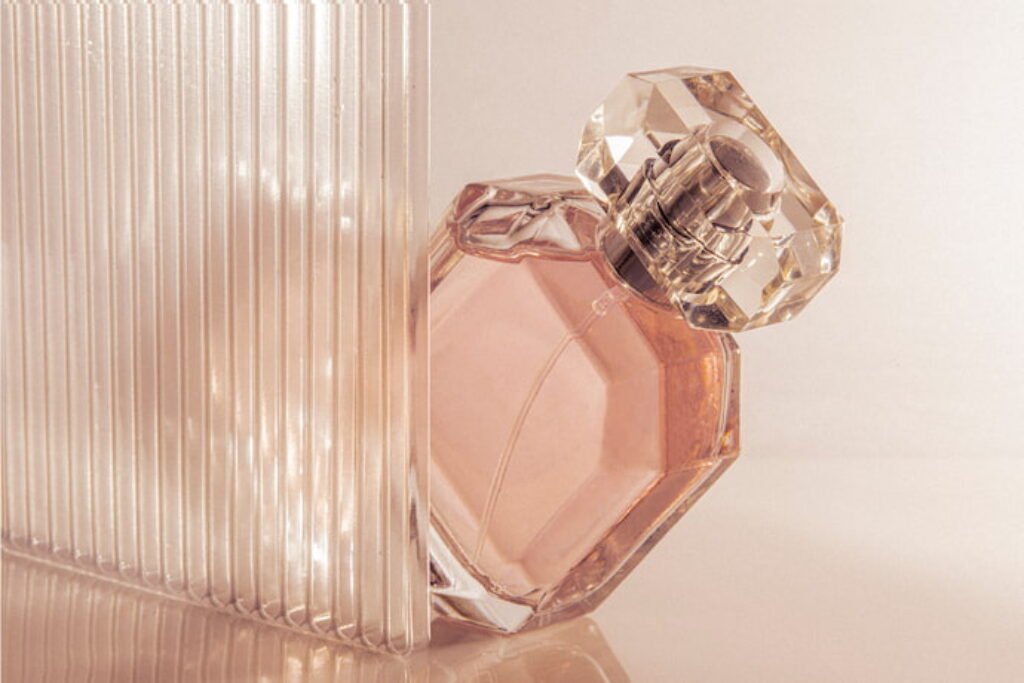 Perfume de frasco rosa em um cenário em tons pastéis.