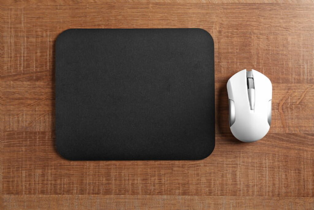 Mouse sem fio branco posicionado ao lado de um mousepad preto.