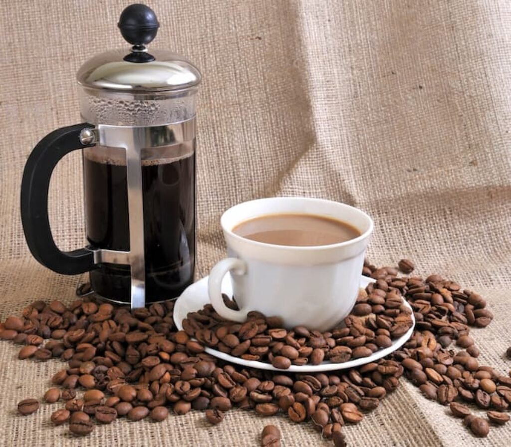 Grãos de café, uma xícara e uma prensa francesa.