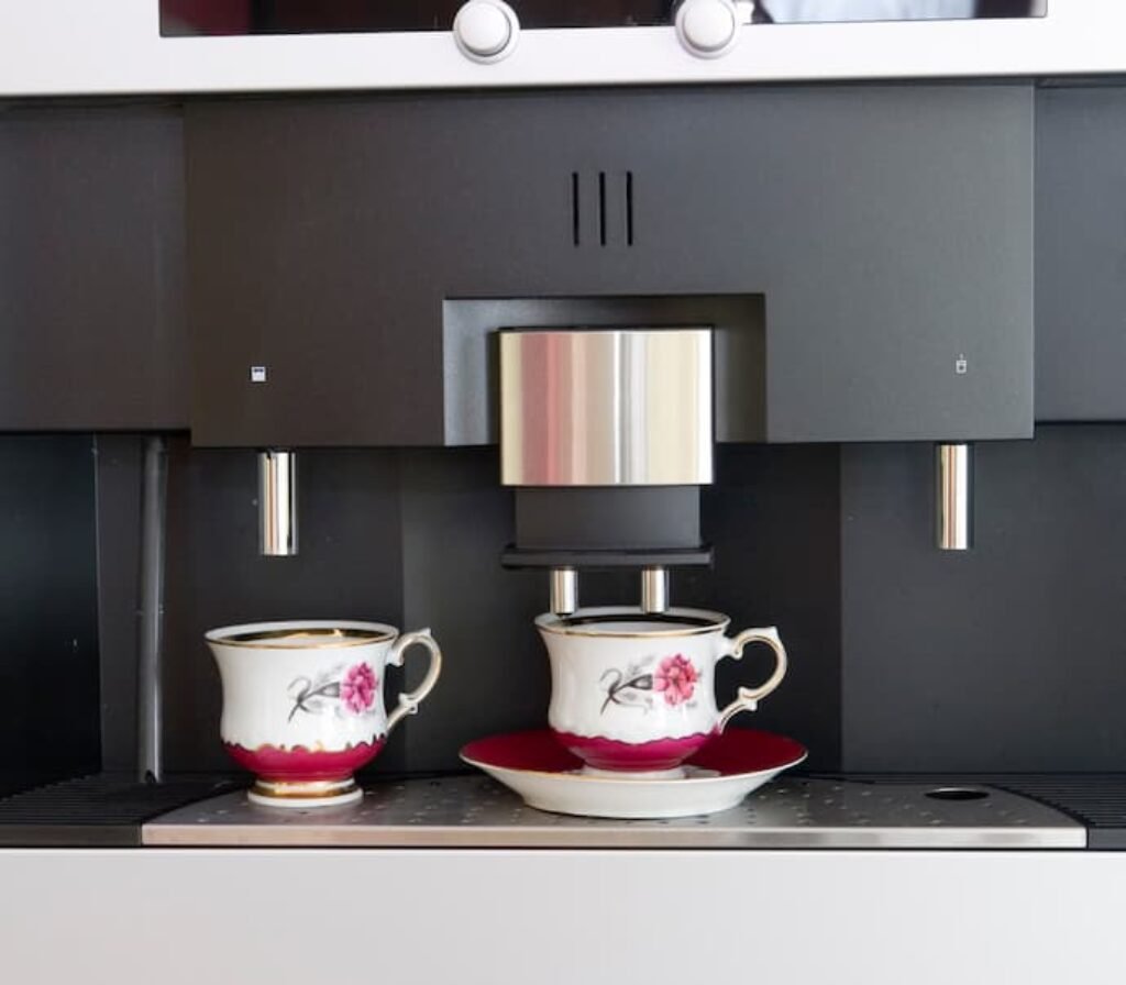 Uma cafeteira moderna com gancho duplo e duas xícaras de café.