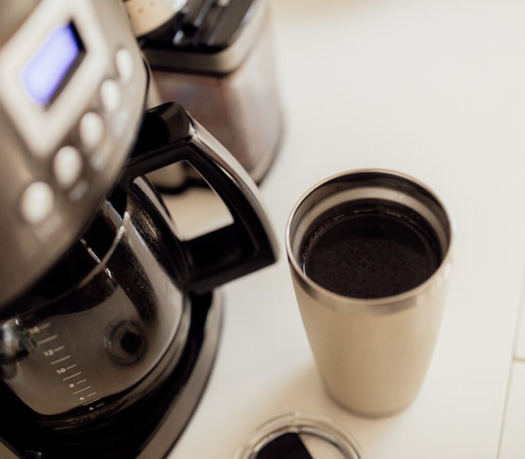 Um copo grande de inox ao lado de uma melhor cafeteira expresso.