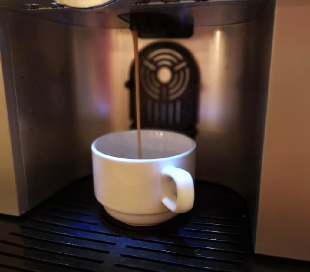 Uma máquina colocando café em uma xícara branca.