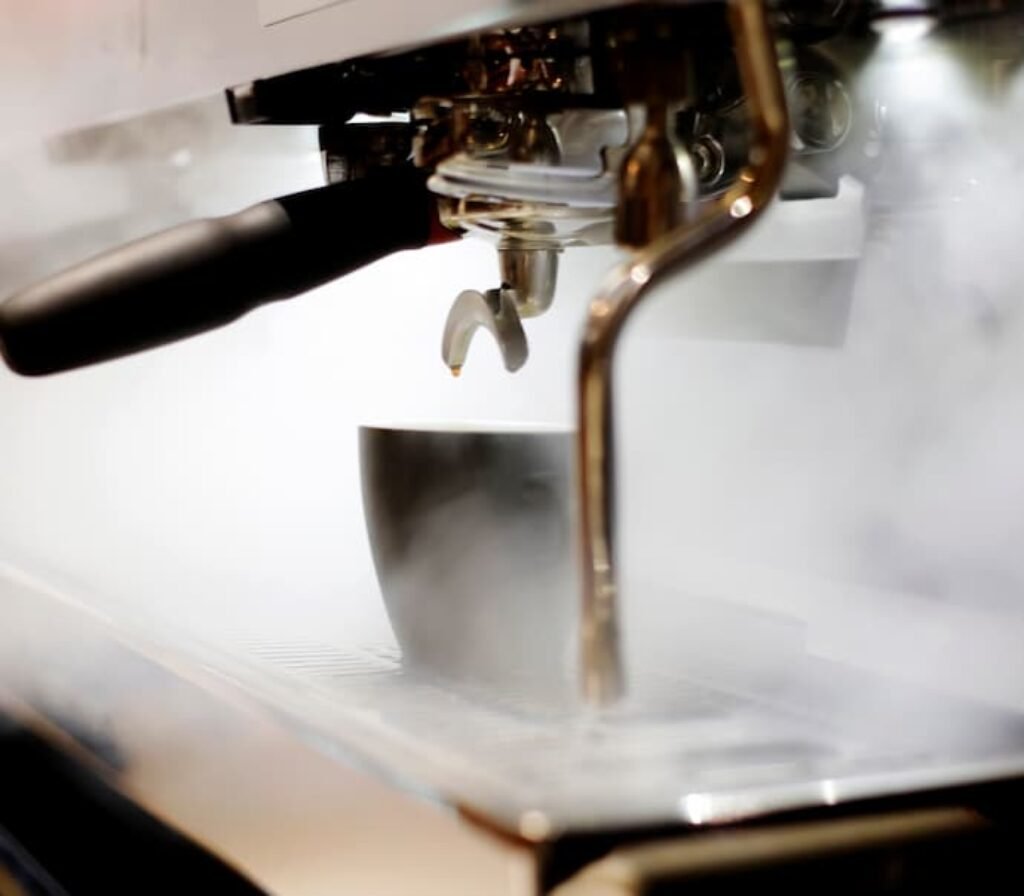 Uma cafeteira expresso soltando vapor antes de servir o café na xícara.