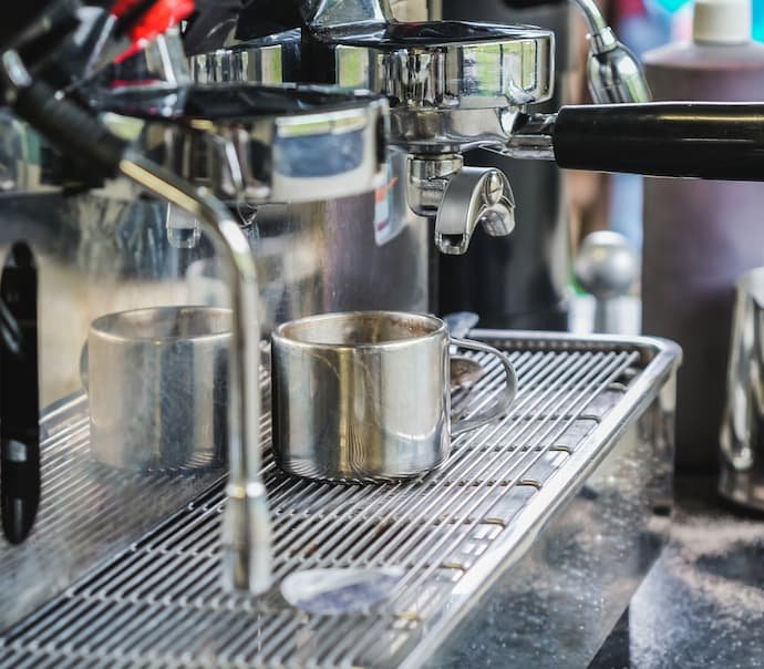 Uma melhor cafeteira expresso de aço inox enchendo de café uma xícara de metal.