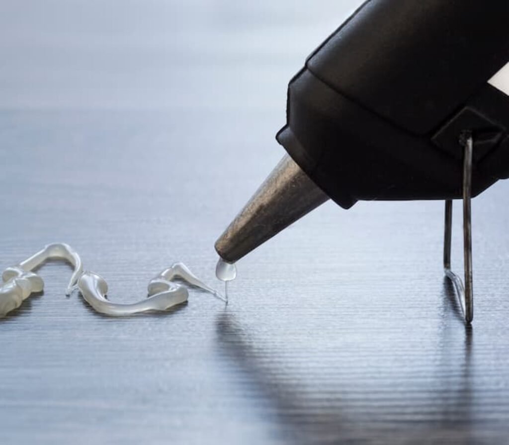 Uma pistola de cola quente com bico de metal derramando cola em uma mesa.