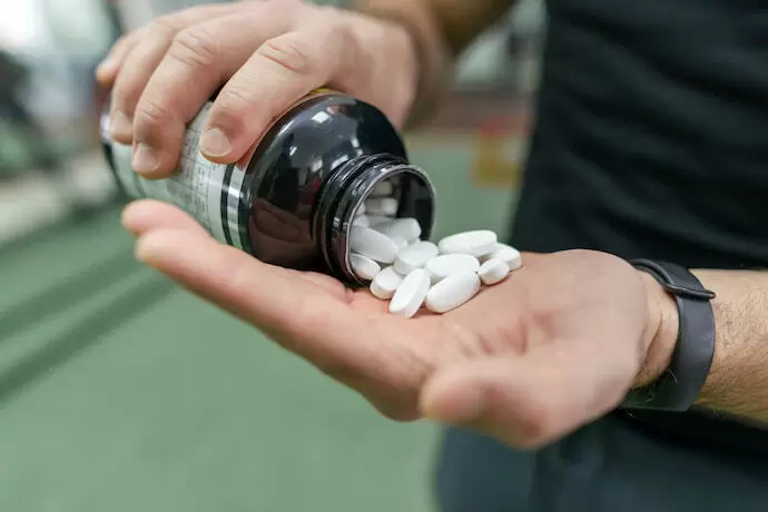 Homem jogando comprimidos de BCAA na mão.