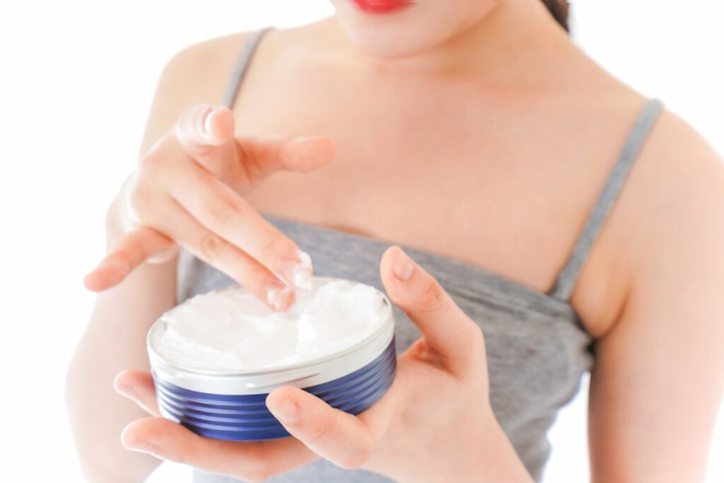 Mulher pegando creme hidratante com a mão.