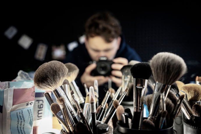 Homem fotografando um estojo de maquiagens.