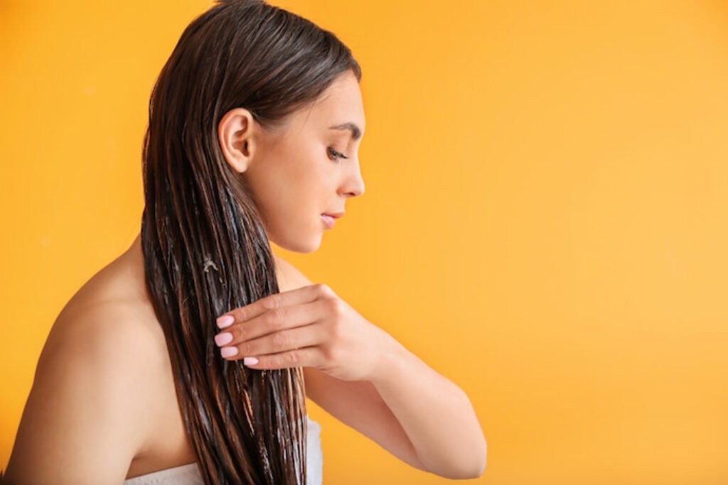 Mulher passando óleo no cabelo liso em um fundo amarelo.