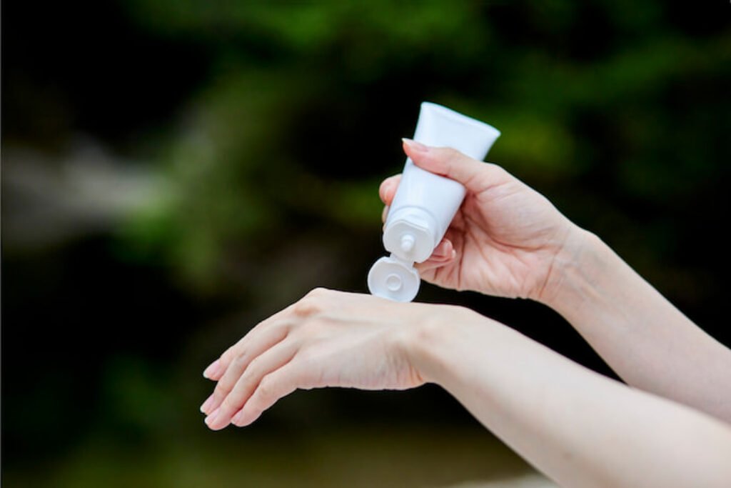 Pessoa colocando bronzeador na mão.