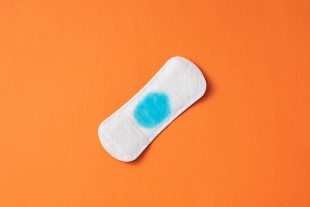 Absorvente aberto com uma mancha azul em um fundo laranja.